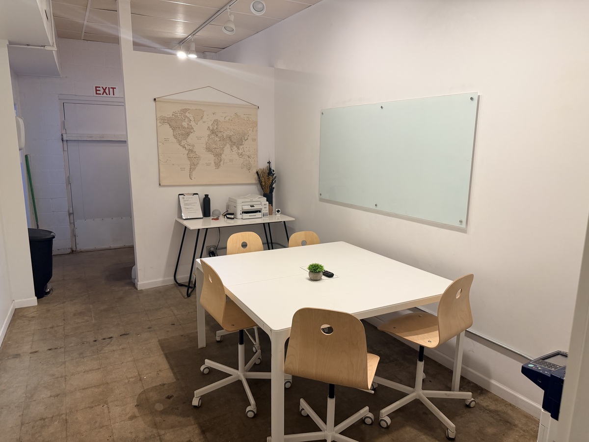 The Meeting Room Annex, a small semi-private room with a white table, four chairs and a glass whiteboard